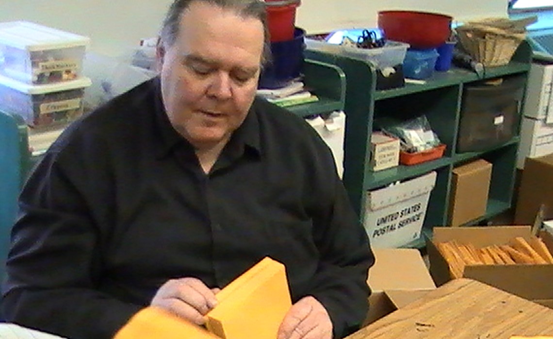 Mr. Paul at his desk, surrounded by shelves of crayons and markers